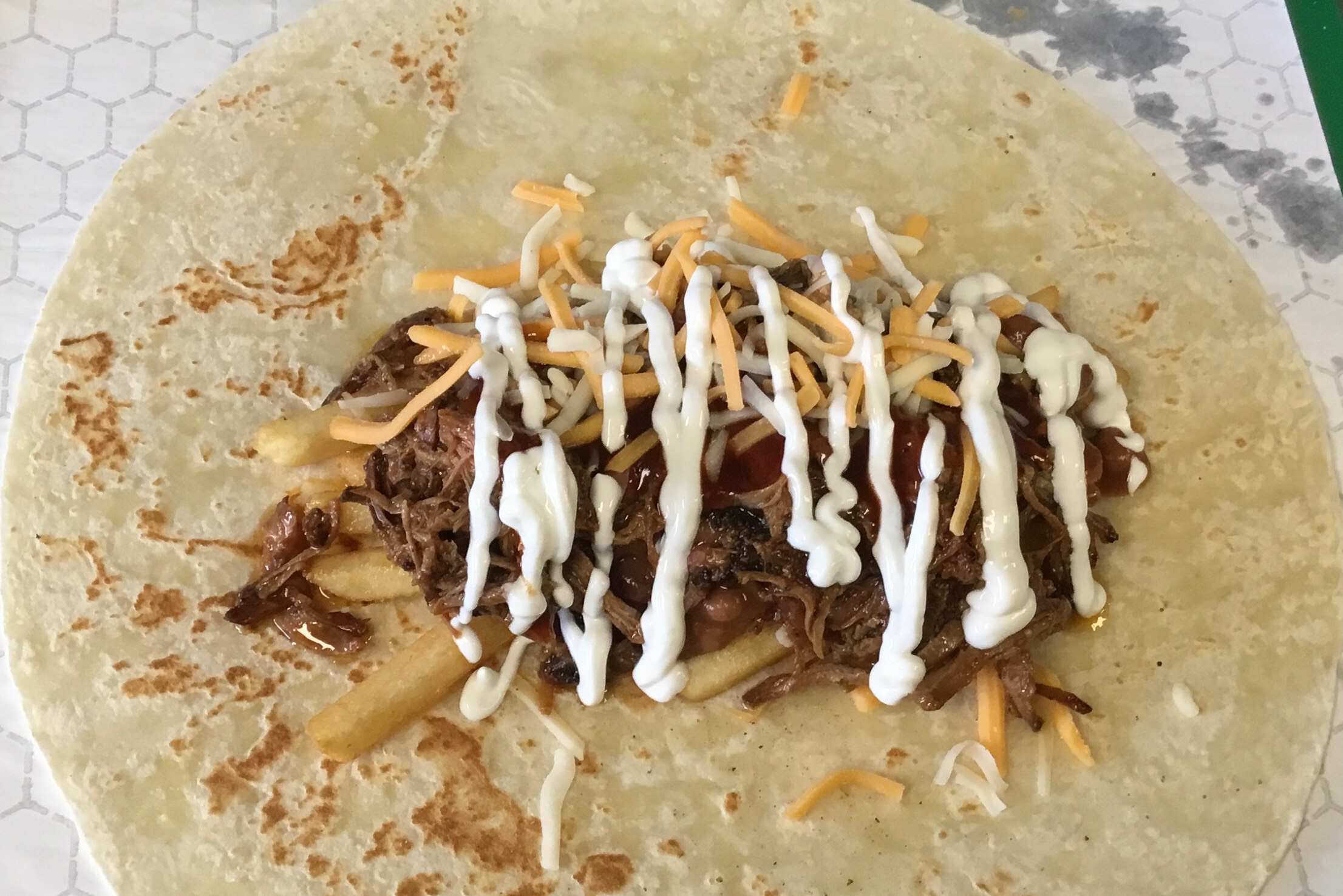 Crispy fries topped with shredded cheese, pinto beans, choice of slow-smoked BBQ meat, BBQ sauce and sour cream.
(Picture shown with ingredients before wrapping and grilling.)