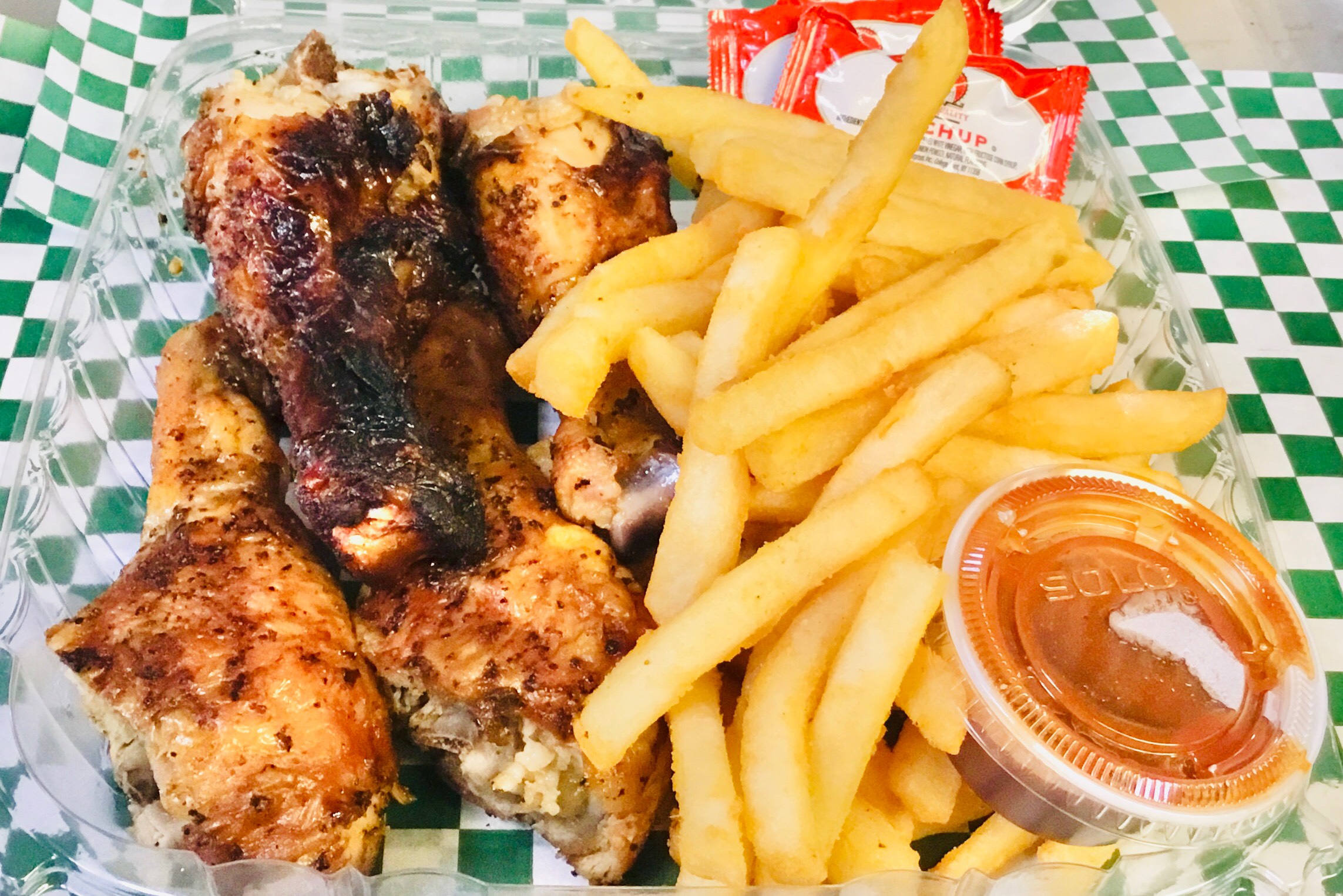 Four chicken drumsticks with a side of BBQ sauce and fries.