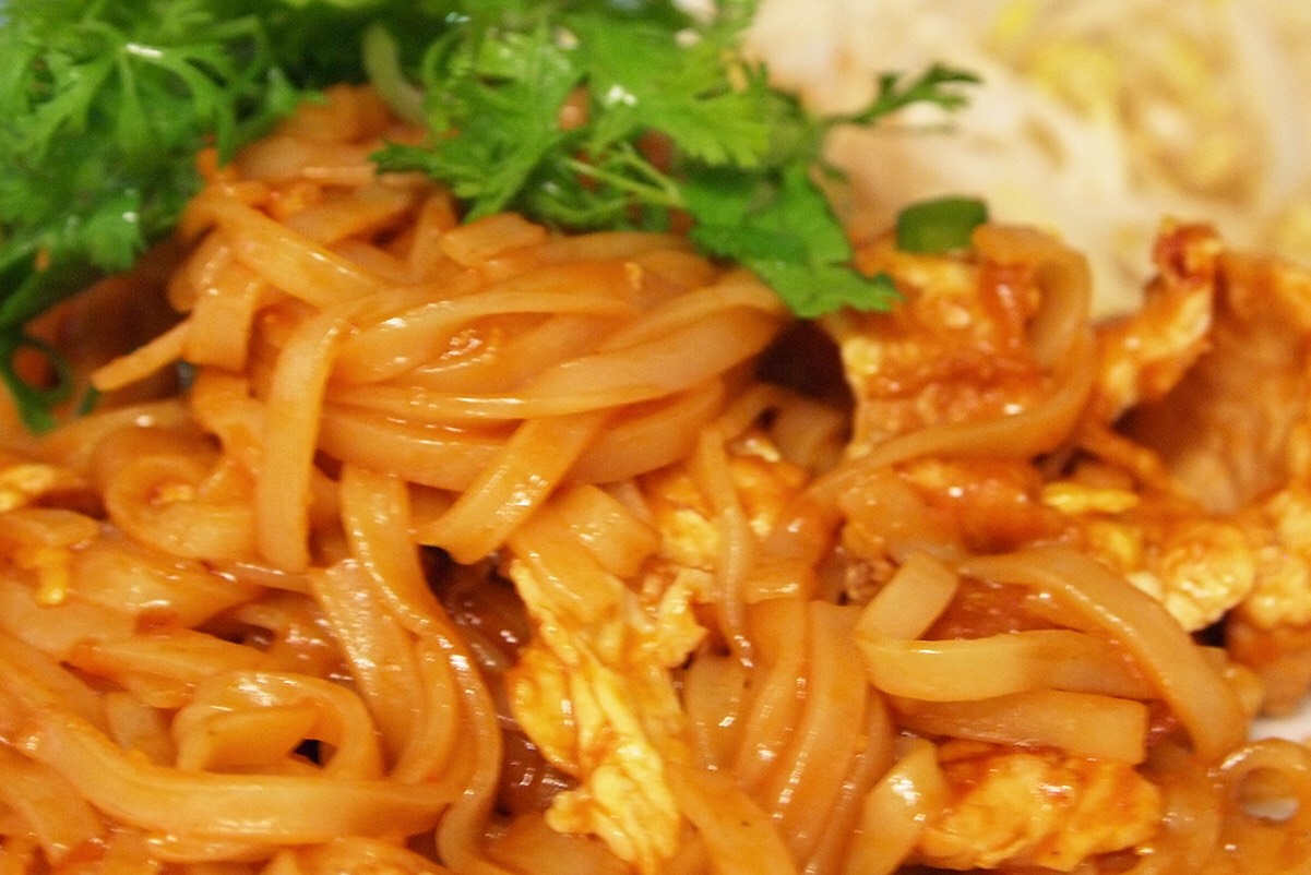 Stir-fried rice noodles tossed with chicken and egg garnished with fresh bean sprouts, cilantro and peanuts